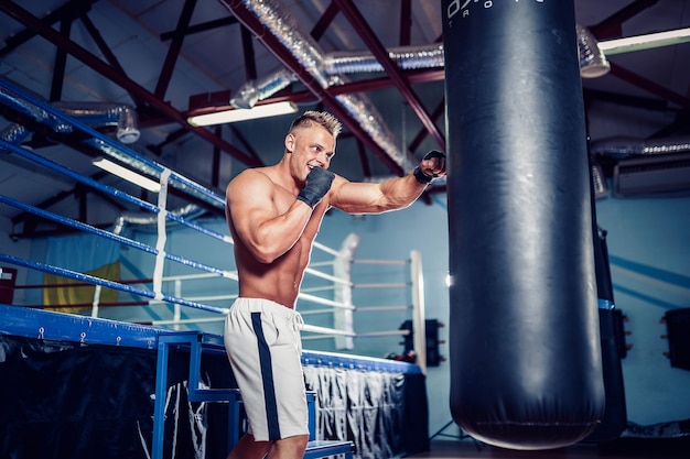 Boxeador masculino treinando com saco de pancadas no escuro salão de esportes. Jovem boxeador treinando no saco de pancadas.