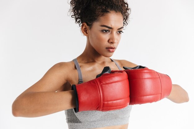 boxeador de la mujer africana de la aptitud de los deportes asombrosos joven hermosa que presenta aislada sobre la pared blanca en guantes.