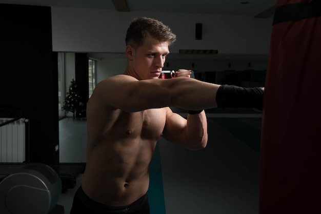 Boxeador muscular descamisado con el saco de arena en gimnasio