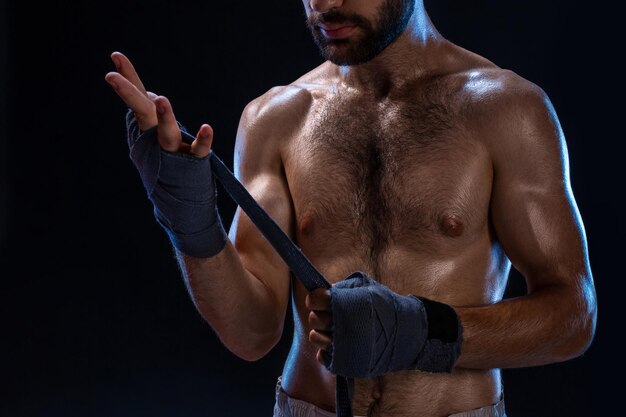 Boxeador preparando sus guantes para una pelea. Foto de hombre musculoso atando las manos sobre fondo negro.