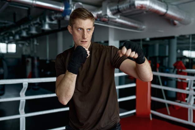 Boxeador profesional con envoltura, vendaje en la mano golpeando aire en el ring en la vista frontal del club de gimnasia deportiva