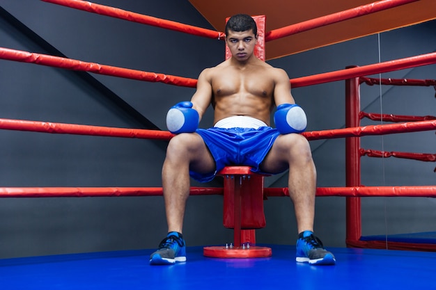 Boxeador profesional masculino sentado en la esquina del ring de boxeo