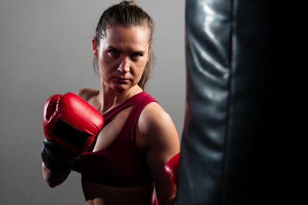 Una boxeadora con un chándal rojo golpea un saco de boxeo en un fondo oscuro