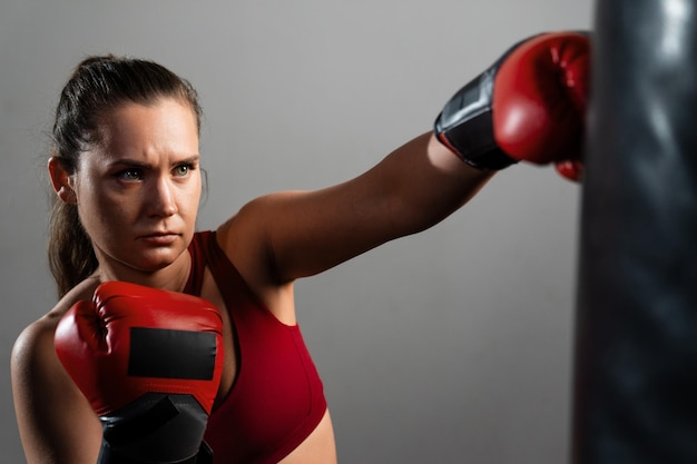 Una boxeadora con un chándal rojo golpea un saco de boxeo en un fondo oscuro