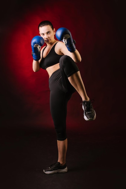 Una boxeadora de deporte extremo con guantes de boxeo azules sobre fondo rojo oscuro