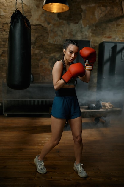 Boxeadora practicando golpes con guantes de boxeo mirando concentrada y con confianza