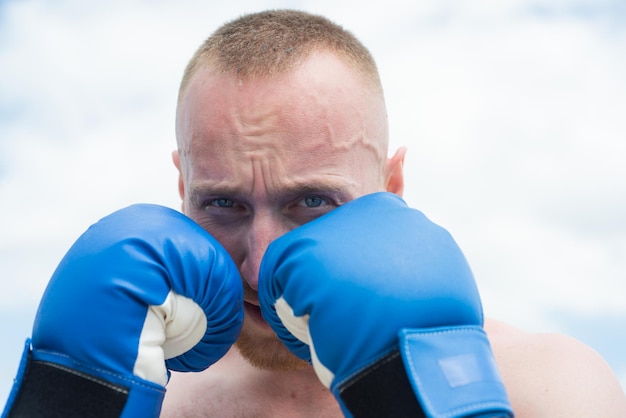 Boxeo deportivo Retrato de primer plano de boxeador deportista peleando en el fondo del cielo Hombre atlético fuerte con guantes de boxeo perforando