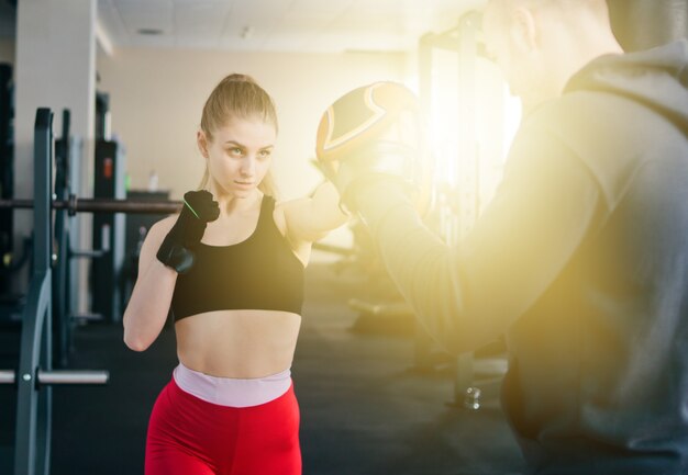 Boxeo femenino joven en el gimnasio con instructor masculino. Pareja, ejercitar, puñetazos