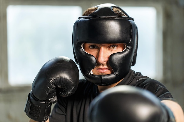 Boxer de retrato vestido com máscara de camiseta preta e luvas de boxe nas mãos em posição de luta em local industrial vazio