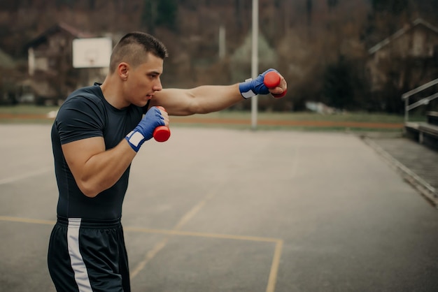 Boxer jovem bonito praticando boxe de sombra com halteres