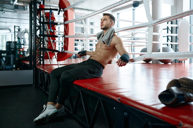 Boxer masculino musculoso sentado na esteira do ringue de boxe