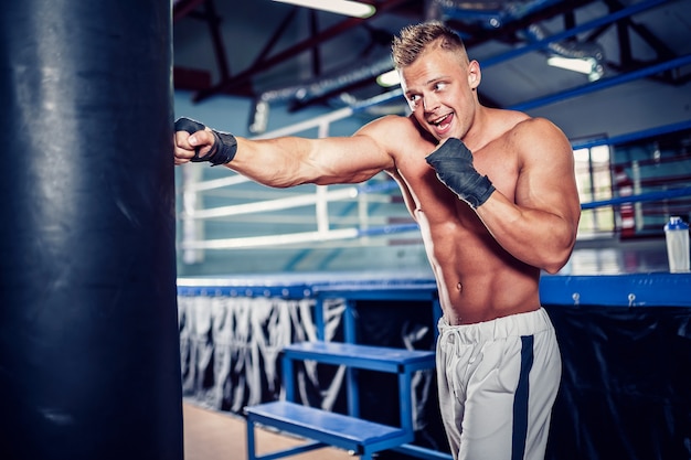 Boxer masculino treinando com saco de pancadas no pavilhão desportivo escuro.