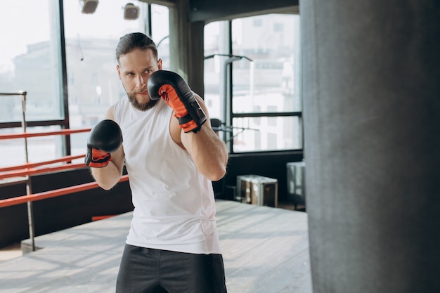 Boxer schlägt Boxsack in der Turnhalle in der Zeitlupe. Junger Mann, der zuhause ausbildet. Starker Athlet im Fitnessstudio