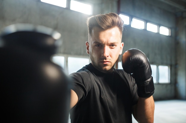 Boxer tailandês vestido com camiseta preta e luvas de boxe nas mãos em local industrial vazio