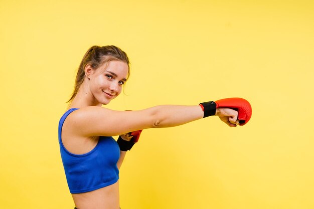 Boxerin in Handschuhen trainiert auf grau-gelbem Hintergrund im Studio.