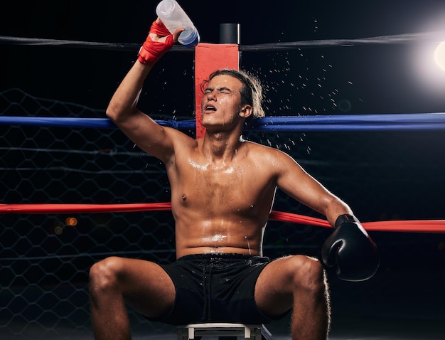 Boxsportler mit Wasserflasche müde nach dem Training oder Training in einem Ring Professioneller Boxer ruht und hydratisiert nach Fitness mma muay thai oder Kampfübungen, Match und Kampf