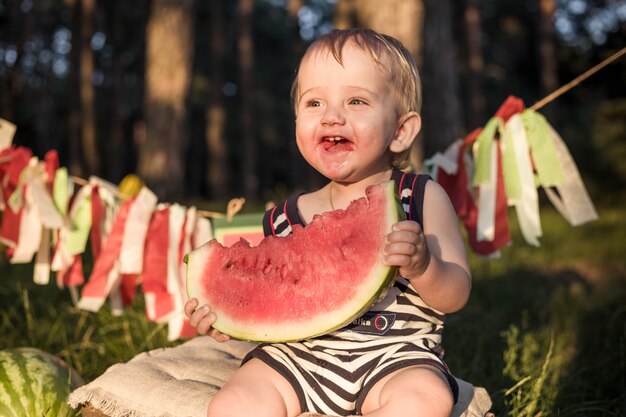 Boy blond sitzt von Wassermelonen an einem Sommertag umgeben