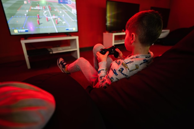 Boy gamer play gamepad consola de videojuegos de fútbol en la sala de juegos roja