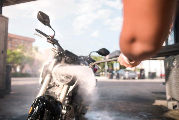 Foto braço de mulher segurando a motocicleta de lavagem de pistola de pressão com água e sabão de pressão em um posto de gasolina.