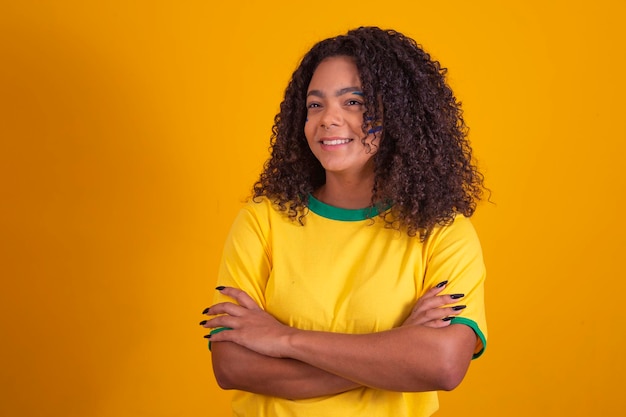 Foto braços de fã de futebol brasileiro jovem negro cruzados sobre o corpo linda líder de torcida brasileira com braços cruzados sobre fundo amarelo