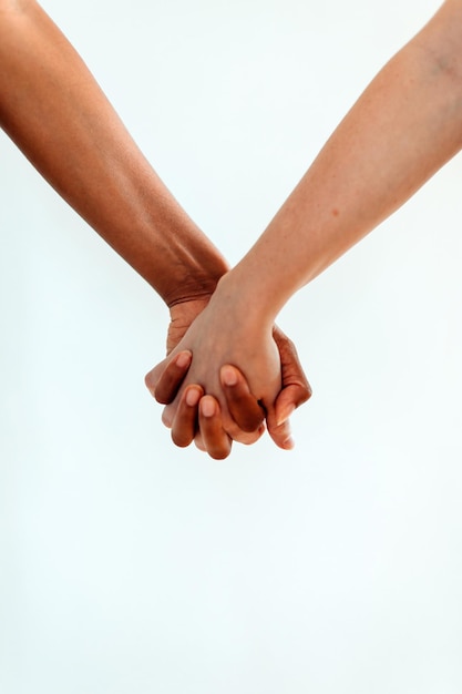 Braços femininos de casal multiétnico de mãos dadas contra o fundo branco