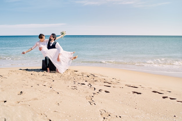 Bräutigam hält Braut in seinen Armen bei einer Strandhochzeit an der Küste