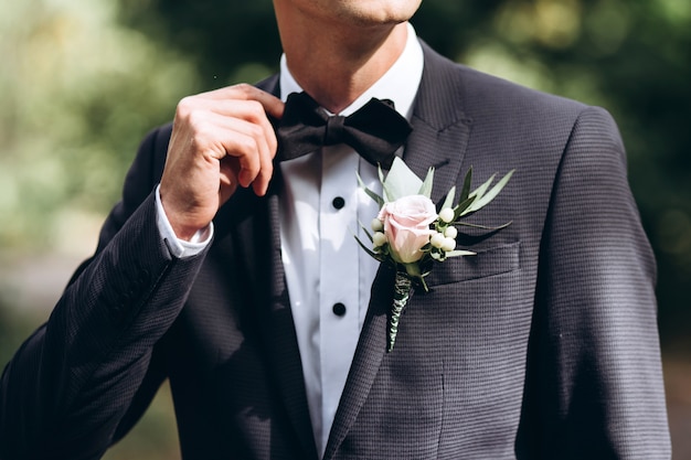 Bräutigam im Anzug glättet seine Krawatte Bubochku. Boutonniere am Revers seiner Jacke. junger Mann in einem Business-Anzug.