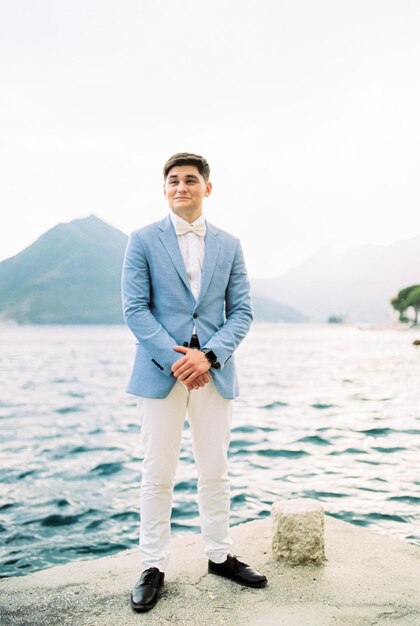 Bräutigam im Anzug steht auf dem Pier vor der Kulisse der Berge