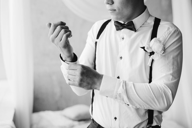 Bräutigam Morgenvorbereitung Gutaussehender Bräutigam in Hosenträgern mit Schleife, der sich anzieht und sich auf die Hochzeit im Hotel vorbereitet. Der Bräutigam trägt Manschettenknöpfe in einem weißen Hemd, Schwarz-Weiß-Porträt