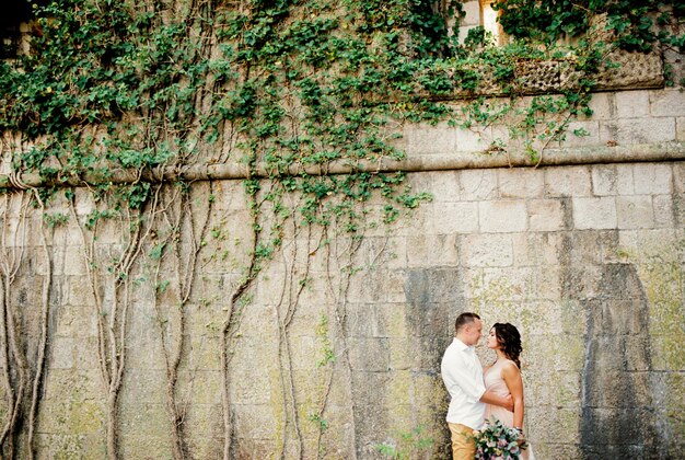 Bräutigam umarmt Braut in der Nähe der Steinmauer des alten Gebäudes mit von Efeu bewachsenen Fenstern