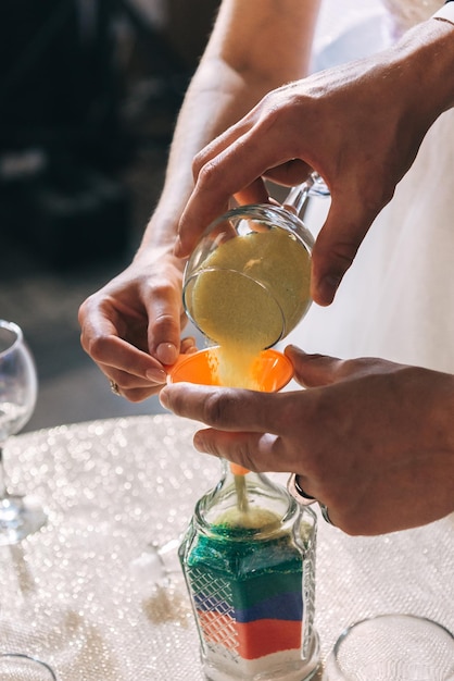 Bräutigam und Braut füllen farbigen Sand in die Flasche