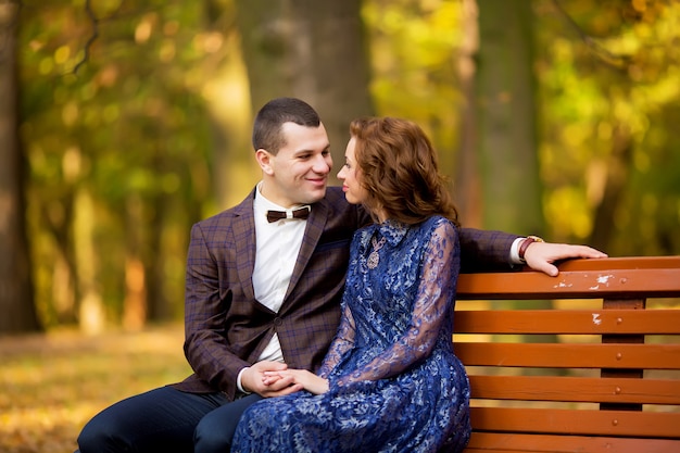 Bräutigam und Braut sitzen auf Bank in einem Park. Lächeln Hochzeitskleid.