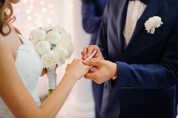 Bräutigam zieht einen goldenen Ehering am Finger einer Braut in einem weißen Kleid an