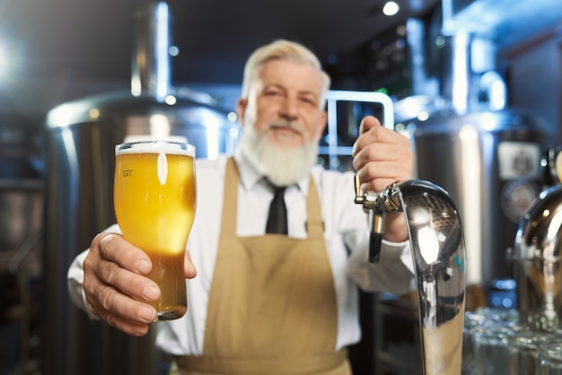 Foto braga idoso segurando copo frio com cerveja lager