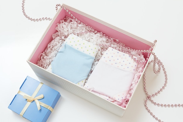 Bragas de algodón dobladas de diferentes colores en una caja, abalorios y una caja de regalo en la superficie blanca.