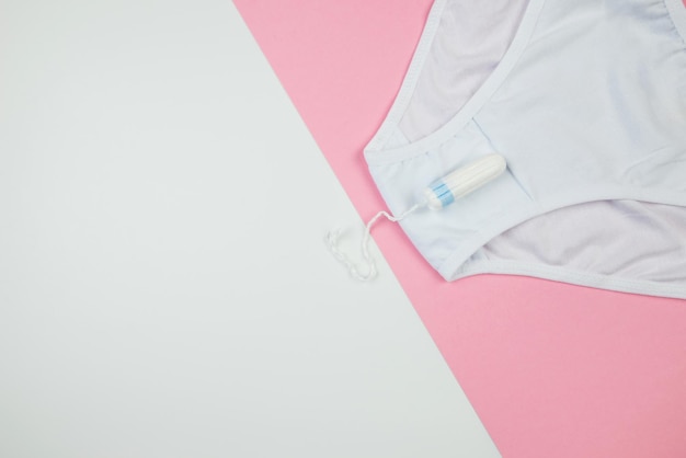 Bragas blancas de tampón para mujer sobre un fondo rosa y blanco con vista superior del espacio de copia