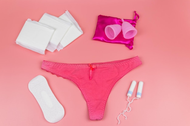 Bragas de mujer con copas menstruales, toallas sanitarias y tampones sobre fondo rosa pastel Vista superior Concepto de higiene femenina de la menstruación de días críticos