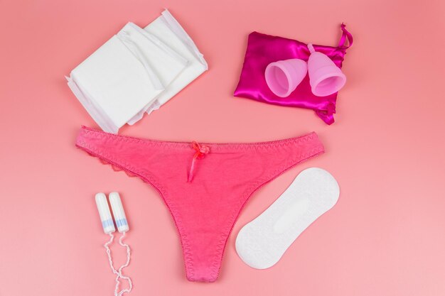 Foto bragas de mujer con copas menstruales, toallas sanitarias y tampones sobre fondo rosa pastel vista superior concepto de higiene femenina de la menstruación de días críticos