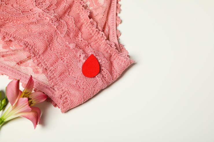 Bragas rosas con una gota roja de menstruación cerca de una flor.