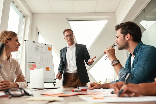 Brainstorming reifer Geschäftsmann in formeller Kleidung, der in der Nähe des Whiteboards steht und etwas erklärt