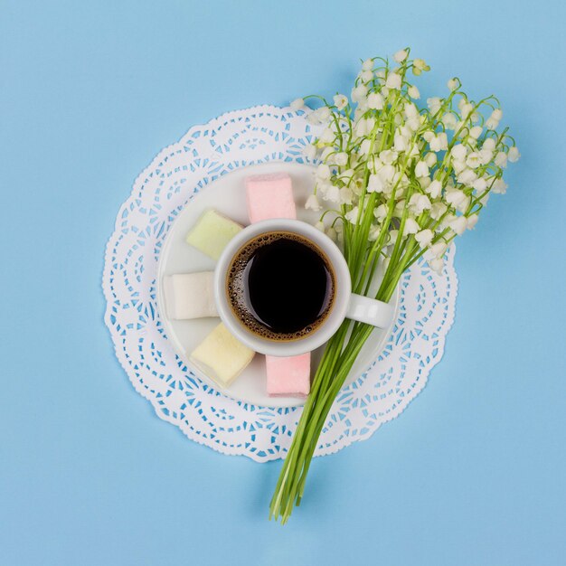 Branca xícara de café com leite em um pires, marshmallow, um buquê de flores de lírio do vale, vista superior plana leigos