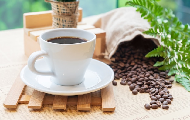 Branca xícara de café preto ou chá na placa de madeira sobre o feijão de café turva