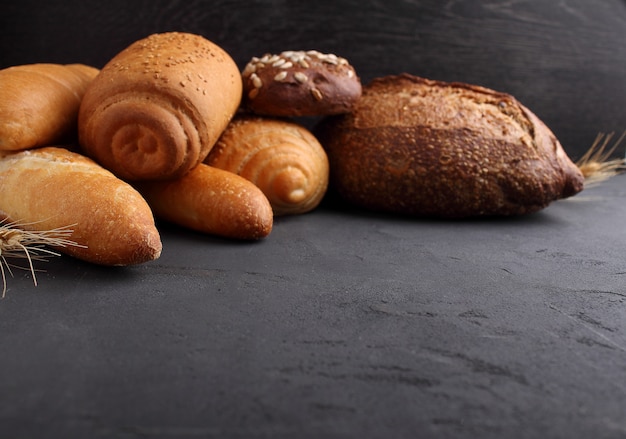 Branco, cinza e pão de centeio, baguete, rolo com sementes de gergelim em um fundo preto