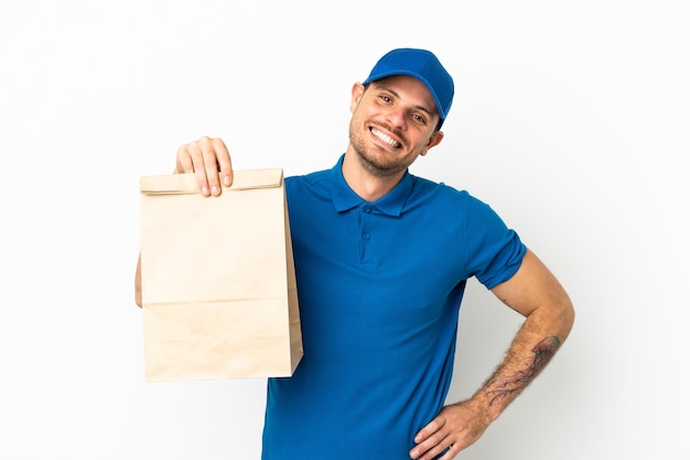 Brasileiro levando uma sacola de comida para viagem isolada no fundo branco posando com os braços na cintura e sorrindo