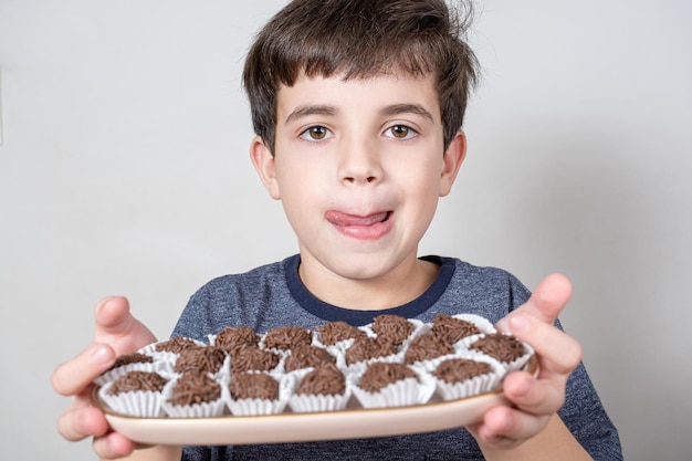 Brasileño de 9 años sosteniendo una bandeja con varias bolas de chocolate brasileño y lamiéndose los labios