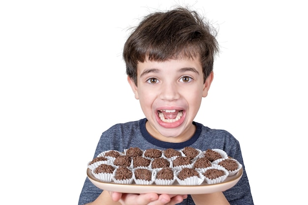 Foto brasileño de 9 años sosteniendo una bandeja con varias bolas de chocolate brasileño y mirando a la cámara con una gran sonrisa