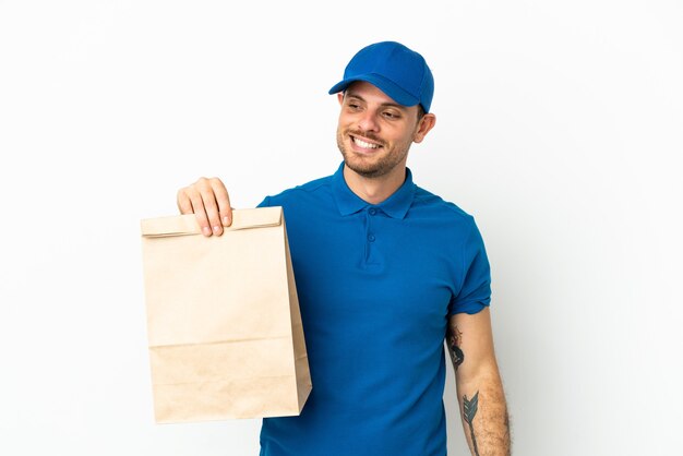 Brasileño tomando una bolsa de comida para llevar aislado sobre fondo blanco mirando hacia el lado y sonriendo