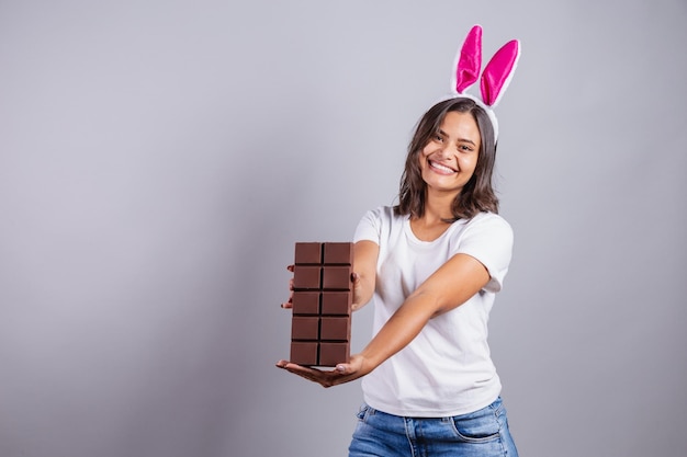 Brasilianerin mit Osterhasenohren lächelt glücklich und hält Osterschokoriegel