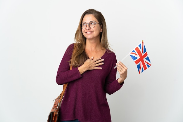 Brasilianische Frau des Mittelalters, die eine Flagge des Vereinigten Königreichs lokalisiert auf weißer Wand hält, die beim Lächeln oben schaut