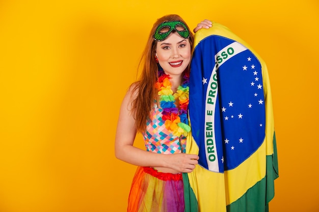 Brasilianische Rothaarige in Karnevalskleidung mit einer Blumenkette um den Hals, die die brasilianische Flagge hält